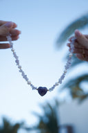 Necklace with a heart-shaped purple bead held by hands against a blurred natural background