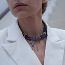 Person wearing a necklace with purple stones.